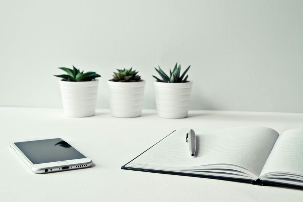 A clean, minimalist workspace featuring a smartphone, open notepad, pen, and potted succulents 